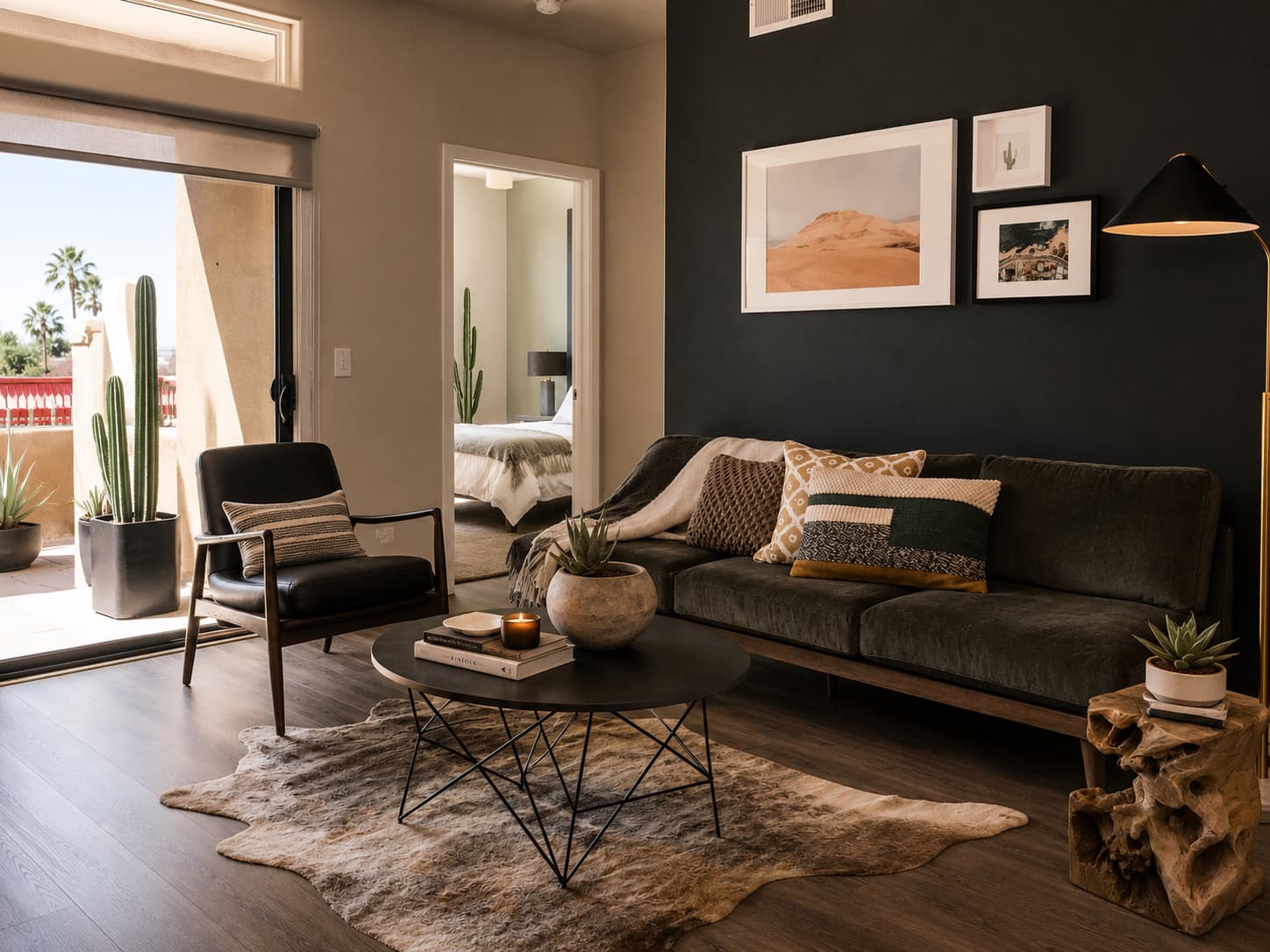 Desert-modern living room with a charcoal accent wall, gallery art, potted cacti, and an open sliding door to a patio